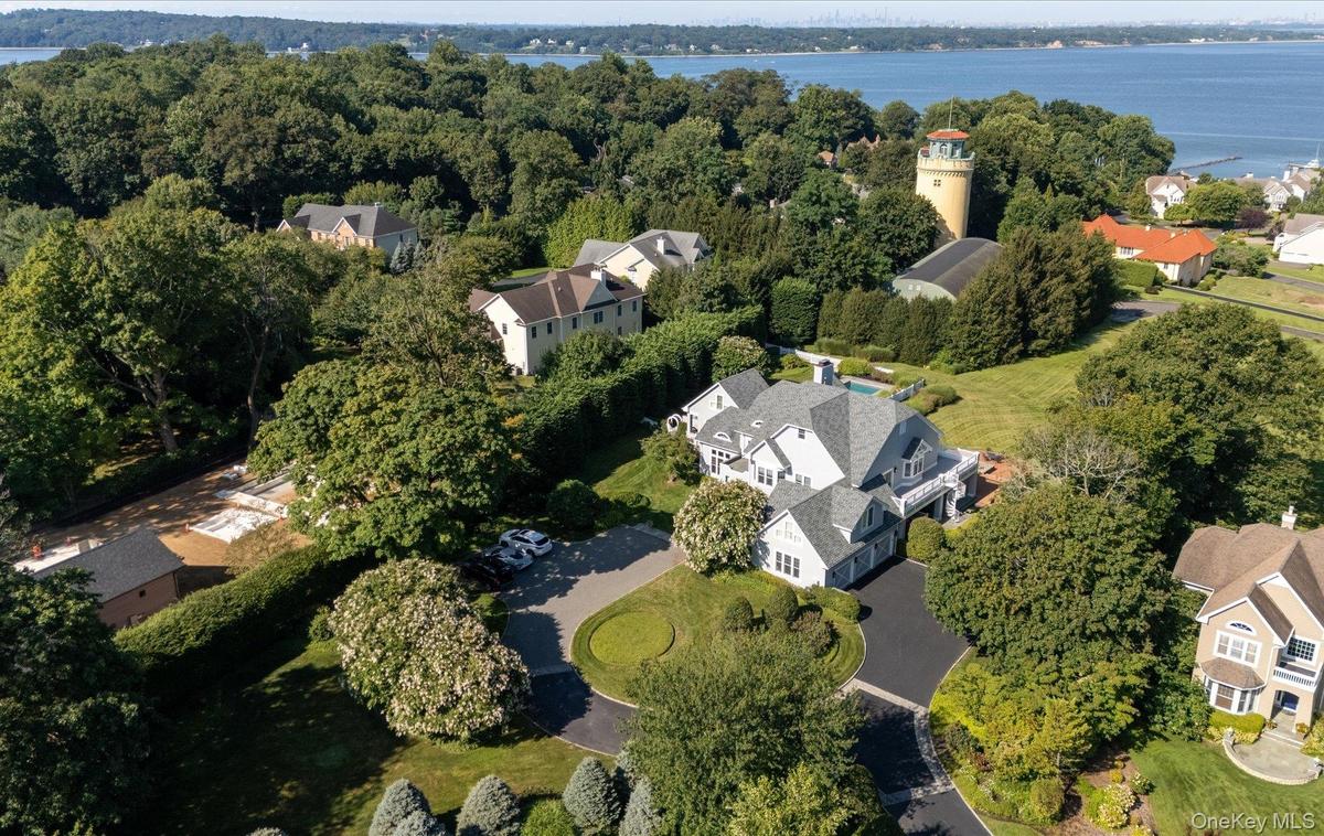 Expansive property featuring a multi-level residence with a gray shingle roof, a circular asphalt driveway, and mature landscaping