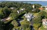 Expansive property featuring a multi-level residence with a gray shingle roof, a circular asphalt driveway, and mature landscaping