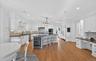 Gourmet kitchen featuring a central island with integrated beverage refrigerator, white cabinetry, dark countertops, and wood-finish flooring