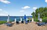 Expansive brick paver patio featuring a clear panel railing with decorative posts, overlooking a body of water with a distant marina