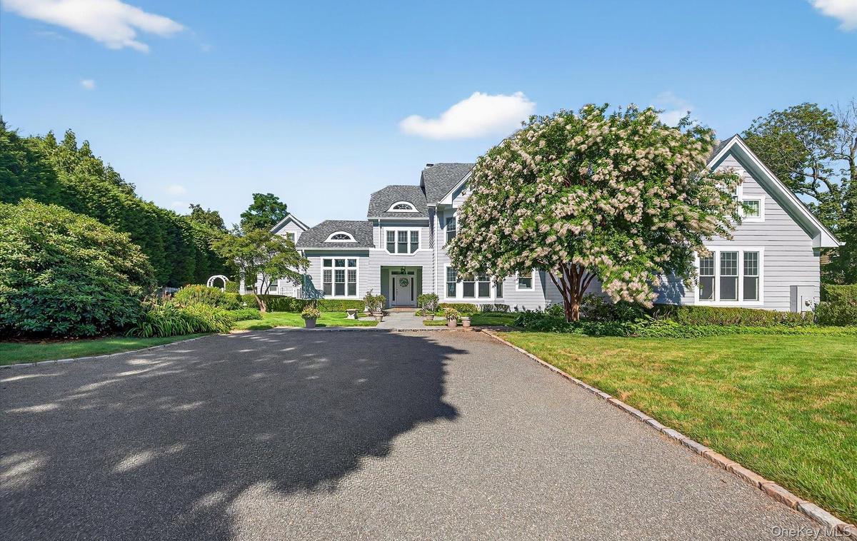 Expansive paved driveway leading to a multi-level residence with light grey siding