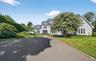 Expansive paved driveway leading to a multi-level residence with light grey siding