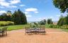 Expansive brick paver patio featuring a fire pit area, surrounded by a manicured lawn and mature landscaping