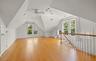Spacious attic room featuring wood-finish flooring, vaulted ceilings, and multiple windows with exterior views