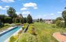 Elongated swimming pool with surrounding hardscaping, a large manicured lawn, a circular paver patio, and mature trees and landscaping