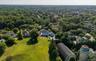Expansive property featuring a meticulously manicured lawn, a large residential structure with a pool, and mature trees
