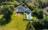 Expansive backyard featuring a rectangular swimming pool, a brick paver patio with a built-in fire pit, and extensive landscaping with mature trees an