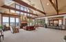 Expansive great room featuring a vaulted ceiling with exposed wood beams, a built-in wet bar, a fireplace with a wood mantle, and floor-to-ceiling win