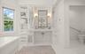 White bathroom featuring a freestanding soaking tub, a vanity with a white countertop and undermount sink, built-in storage cabinetry, a framed mirror