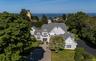 Gray shingle-style residence featuring a multi-gabled roofline, dormer windows, and a paved driveway