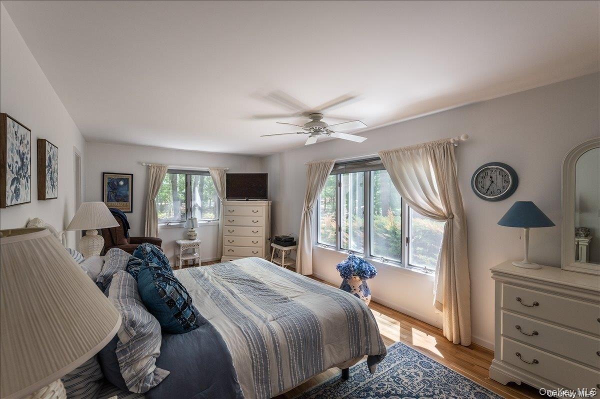Bright bedroom featuring multiple windows, a ceiling fan with integrated lighting, and wood-finish flooring