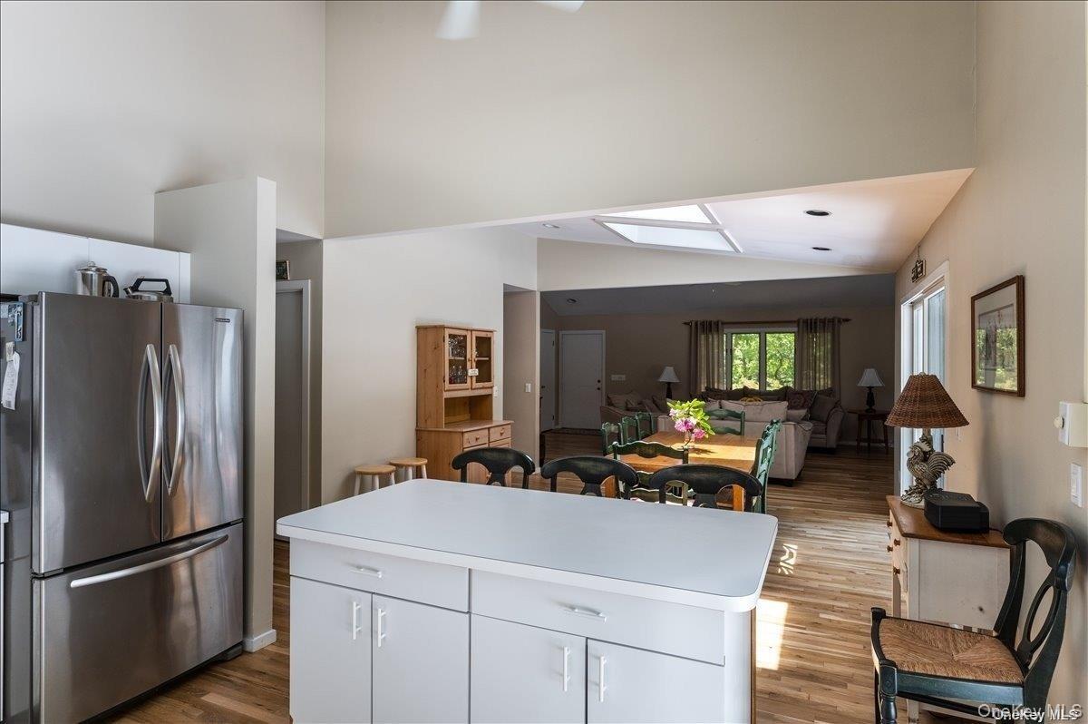 Open-concept kitchen and living area featuring a central island with storage, stainless steel refrigerator, wood-finish flooring, vaulted ceilings, an