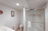 Bathroom featuring a glass-enclosed shower, white vanity with integrated sink, toilet, textured ceiling, and vertical paneling on walls