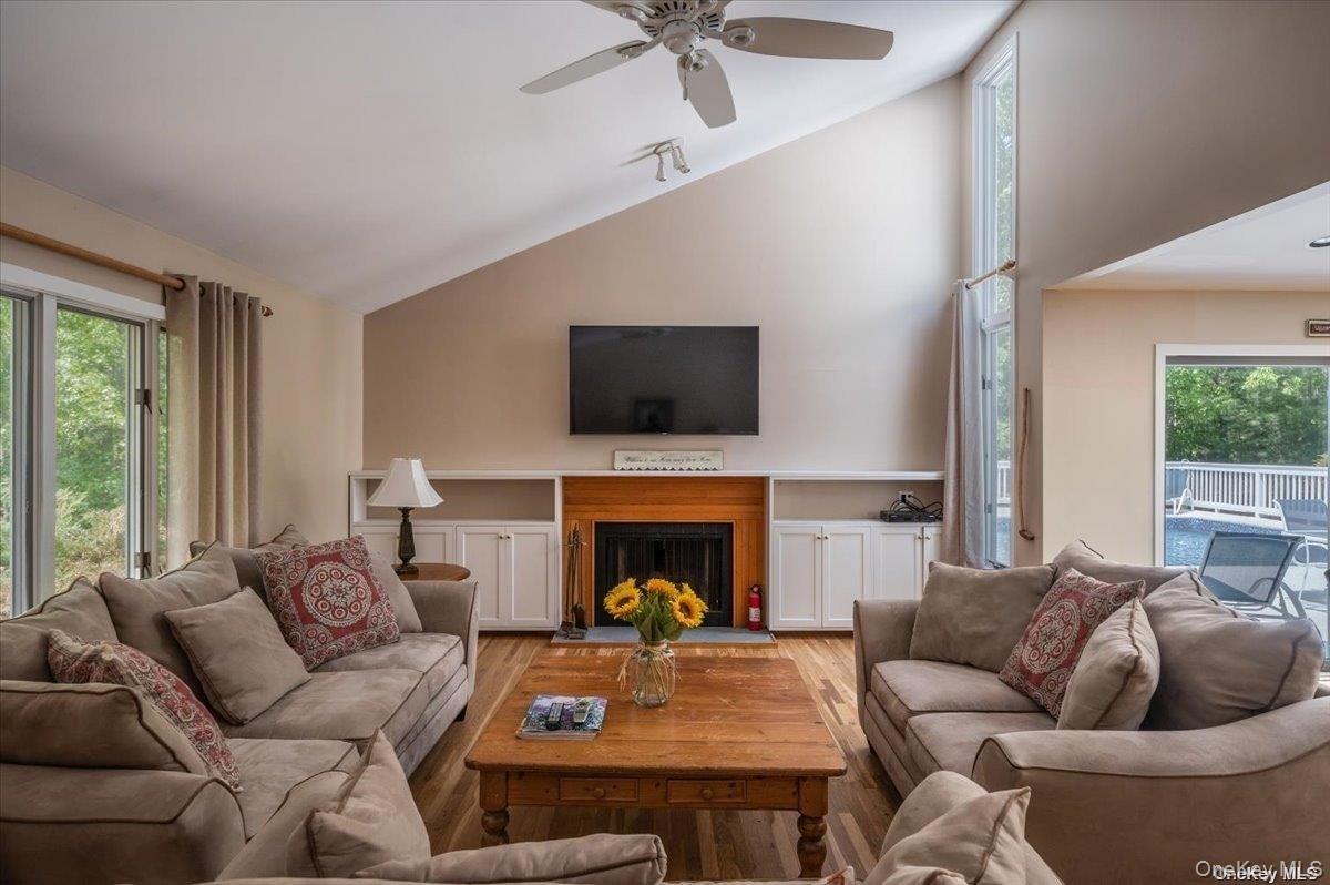 Vaulted ceiling living area featuring hardwood flooring, built-in shelving, a fireplace with a wood mantle, and an outdoor deck with a pool