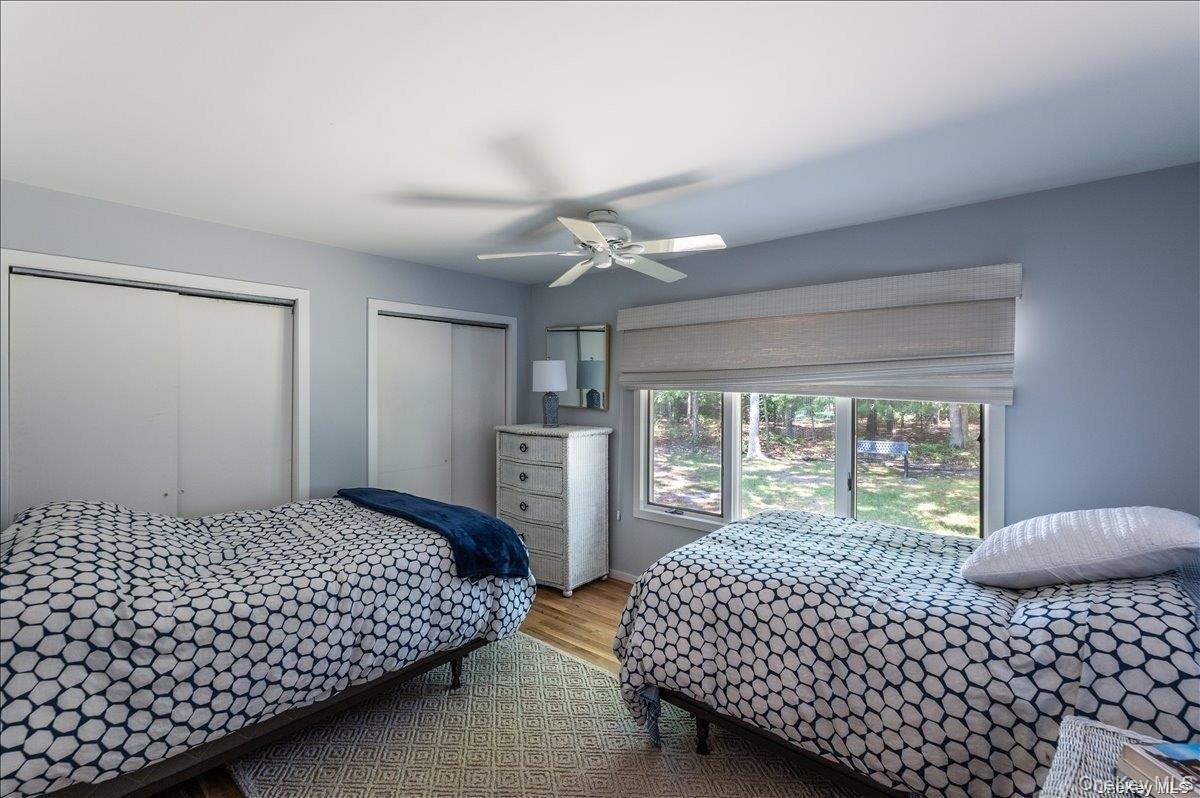 Bedroom featuring wood-finish flooring, two sliding door closets, a ceiling fan, and a large window overlooking the exterior landscape