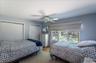 Bedroom featuring wood-finish flooring, two sliding door closets, a ceiling fan, and a large window overlooking the exterior landscape