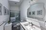 Bathroom featuring a white vanity with an integrated sink and light-toned countertop, a frameless shower-tub combination with sliding glass doors, whi