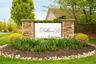 Stone pillars framing a community sign, surrounded by manicured landscaping with flowering plants and green shrubs