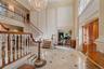 Grand entry foyer featuring a sweeping staircase with detailed balusters and wood handrails, marble flooring with accent inlays, and a multi-tiered cr