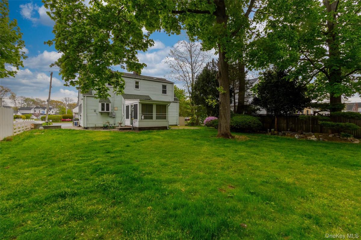 Expansive rear lawn featuring mature trees and a screened-in porch with a panel door