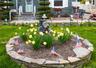 Front yard featuring a stone-lined flower bed with yellow blooms, a manicured lawn, and a paved walkway leading to the entrance