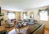 Spacious living area featuring light wood-finish flooring, multiple windows with blinds, a fireplace with a dark hearth, and light-colored walls