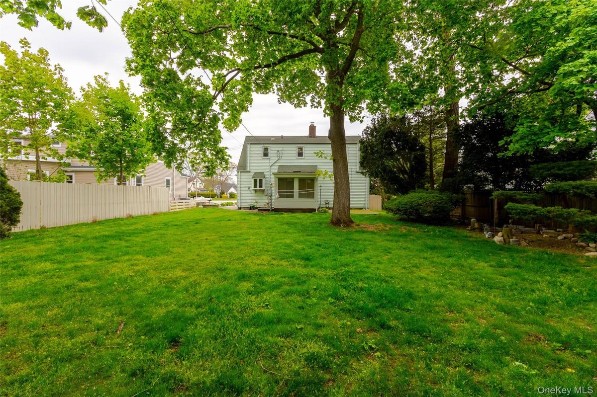 Expansive rear yard featuring a large verdant lawn, mature trees, and a white picket fence