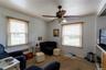 Living area featuring two windows with wood-finish blinds, a ceiling fan with integrated lighting, white vertical paneling on the walls, and carpeted 