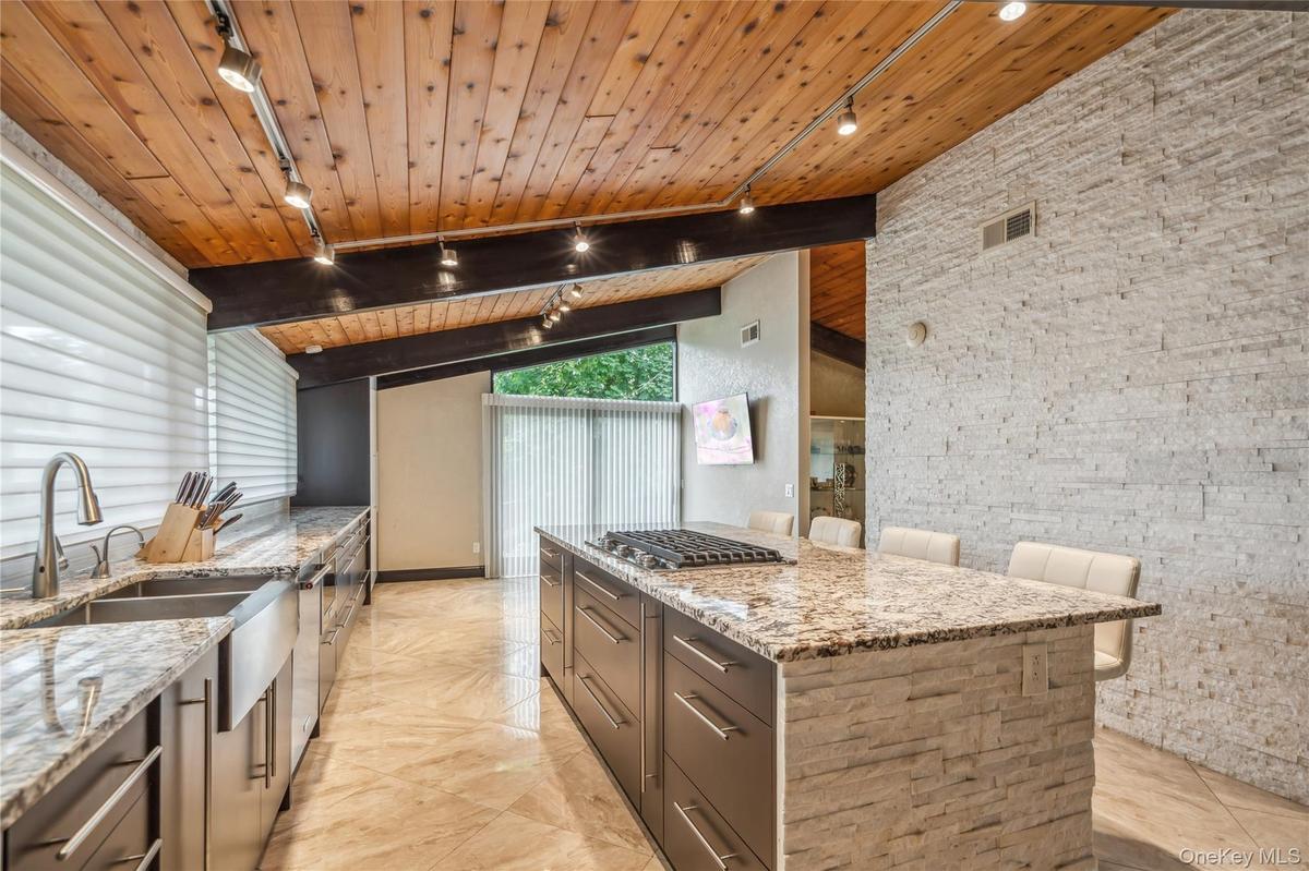 Kitchen with rail lighting, wood ceiling with exposed beams, a sink, light stone counters, and stainless steel gas stovetop