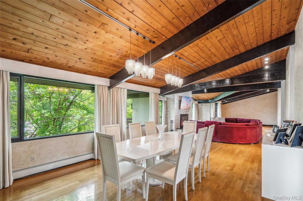 Dining space featuring a baseboard radiator, wooden ceiling with exposed beams, wood finished floors, a chandelier, and a large fireplace