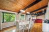 Dining space featuring a baseboard radiator, wooden ceiling with exposed beams, wood finished floors, a chandelier, and a large fireplace