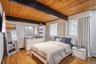 Bedroom with light wood-style flooring and wood ceiling with exposed beams