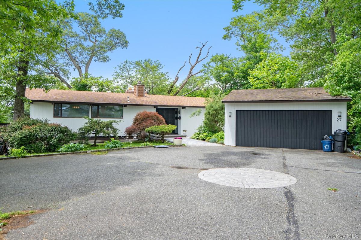 View of front facade featuring driveway, a chimney, and an attached garage