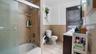 Full bath featuring tile patterned floors, tile walls, bath / shower combo with glass door, vanity, and wainscoting
