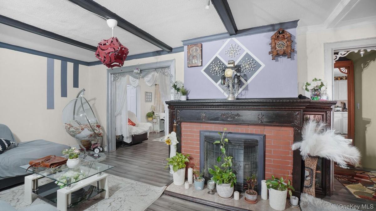 Living area with a brick fireplace, wood finished floors, ornamental molding, and beam ceiling