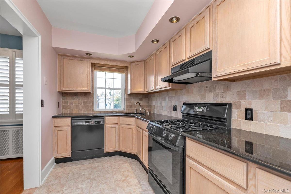 Kitchen featuring light wood-finish cabinetry, black countertops, tiled backsplash, dishwasher, brand new gas range, and recessed lighting.