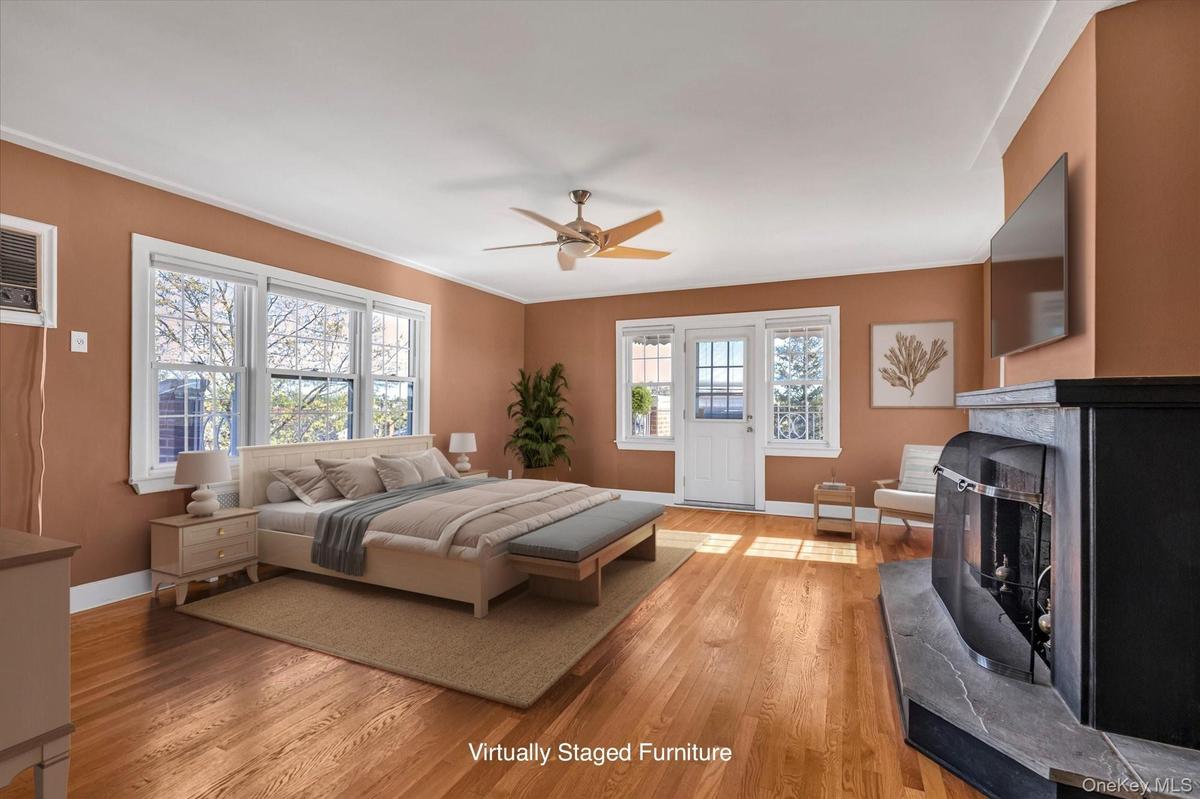 Large Primary Suite featuring hardwood flooring, multiple windows, a ceiling fan, a fireplace, and an exterior door to the rooftop.