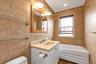 Lower level Bathroom featuring full tile surround, white vanity with integrated sink, gold-toned framed mirror, glass shelving, and a white Ultra Air 