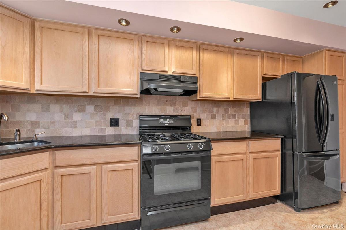 Kitchen featuring light wood cabinetry, dark countertops, tiled backsplash, brand new gas range, brand new LG refrigerator, and recessed lighting.