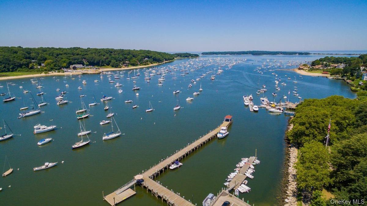 Expansive waterfront setting featuring a long pier with multiple boat slips, a secondary floating dock, and a sandy beach shoreline