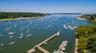 Expansive waterfront setting featuring a long pier with multiple boat slips, a secondary floating dock, and a sandy beach shoreline