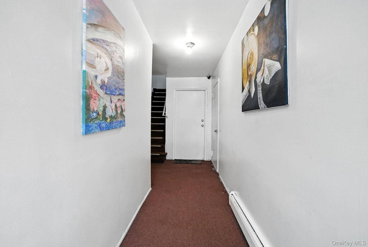 Corridor with dark colored carpet, baseboard heating, and stairway