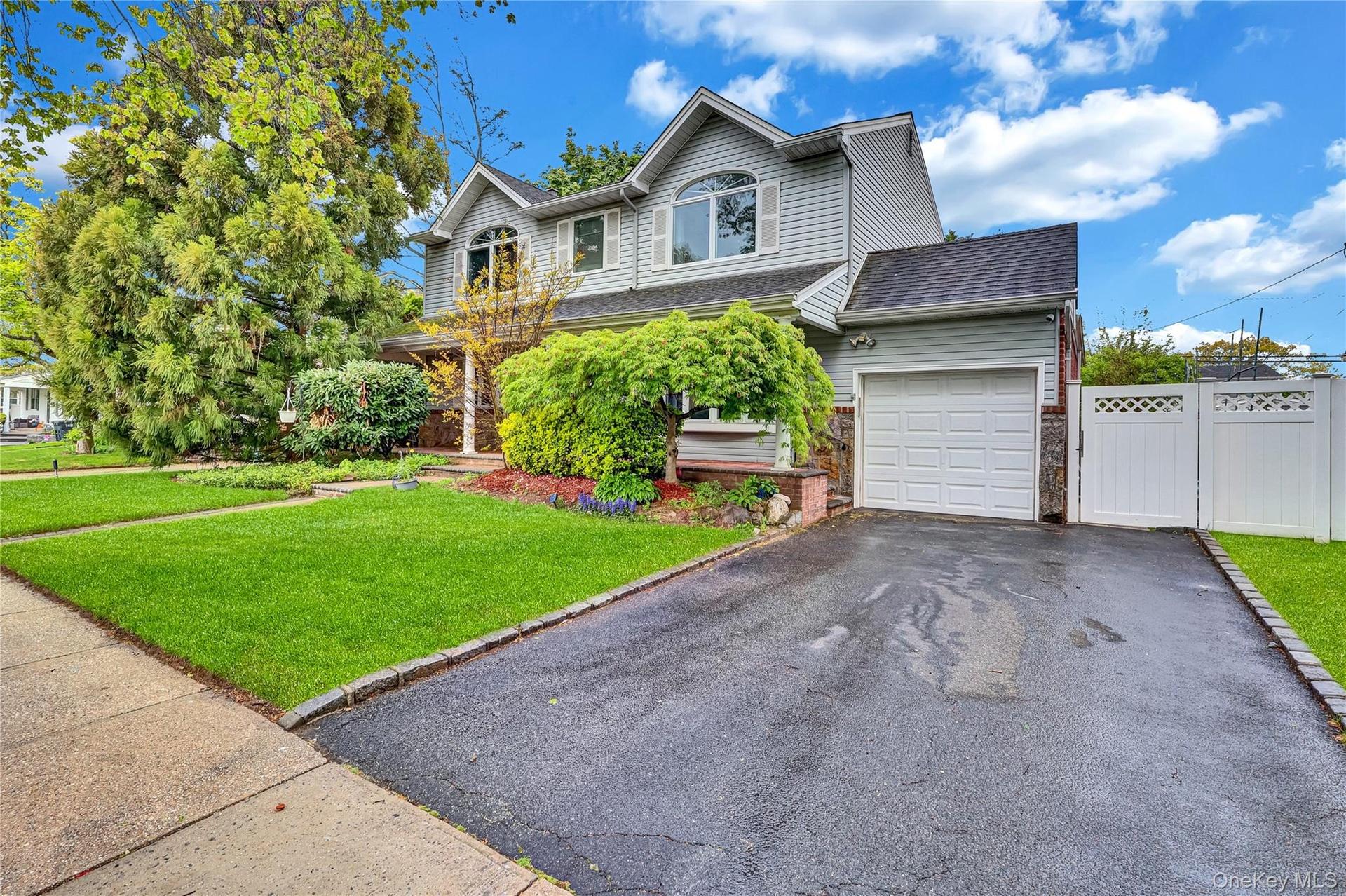 Two-story residence featuring light gray siding, an integrated single-car garage, an arched upper-level window, a paved driveway, and established fron