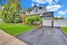 Two-story residence featuring light gray siding, an integrated single-car garage, an arched upper-level window, a paved driveway, and established fron