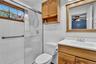 Bathroom featuring a glass-enclosed shower, white tile walls, a window with wood trim, a wood-finish vanity with an integrated sink, and an overhead w