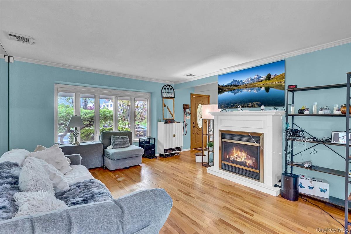 Living area featuring wood-finish flooring, a white mantel fireplace, and a large bay window
