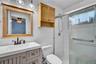 Bathroom featuring white tiled walls, a wood-framed mirror, and a vanity with a white countertop and bronze-finish faucet