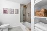 Bathroom featuring a tub with glass shower partition, wall-mounted shower system with brass finishes, tiled shower surround with recessed niche, and b
