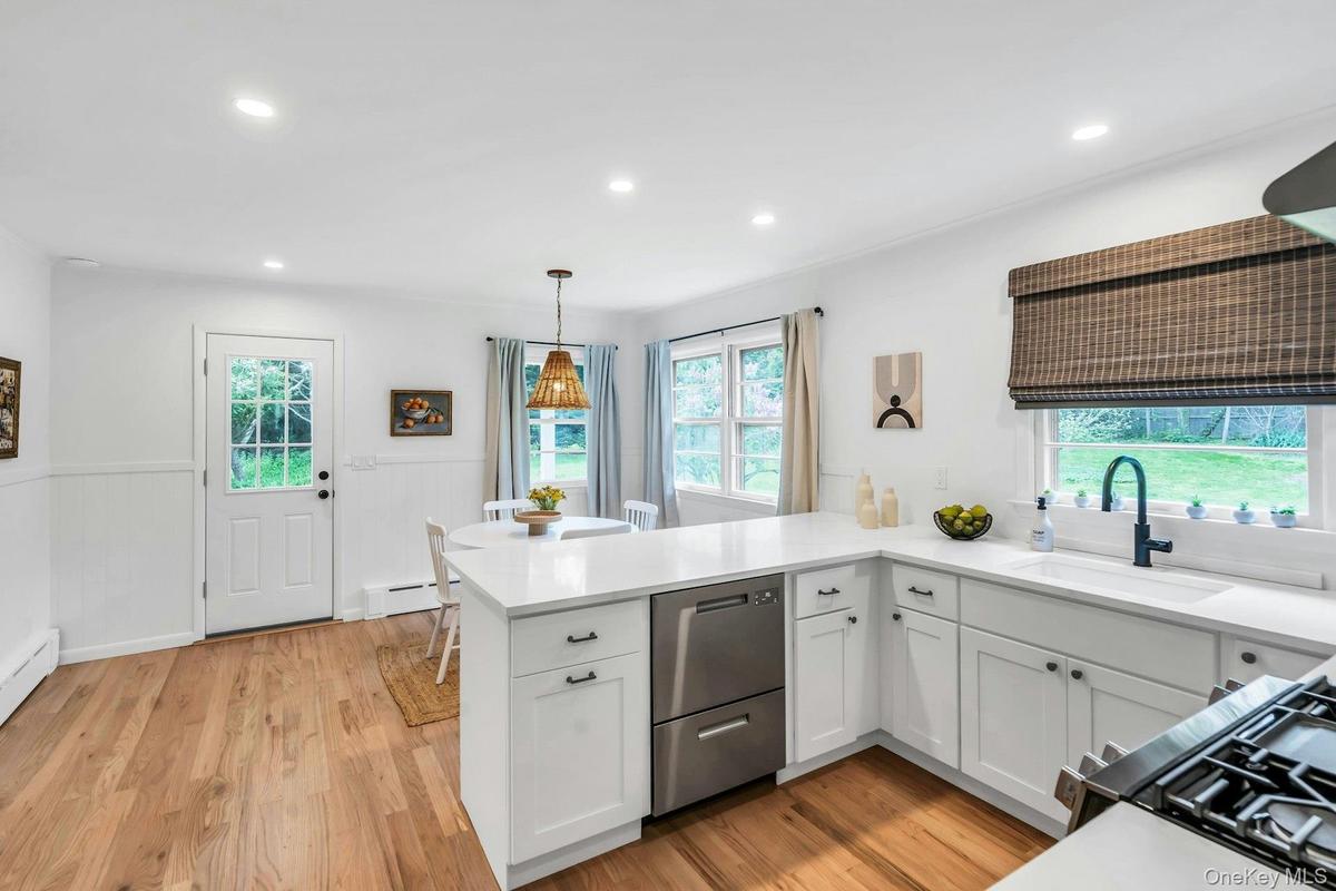 White kitchen featuring wood-finish flooring, white cabinetry with dark hardware, a corner sink with a black gooseneck faucet, a built-in dishwasher, 