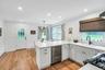 White kitchen featuring wood-finish flooring, white cabinetry with dark hardware, a corner sink with a black gooseneck faucet, a built-in dishwasher, 